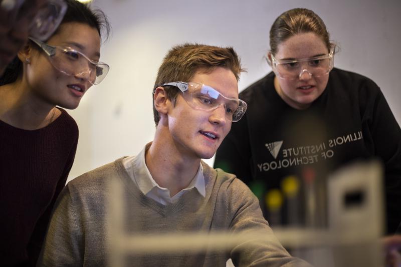 Three students gather around a computer in a chemistry lab